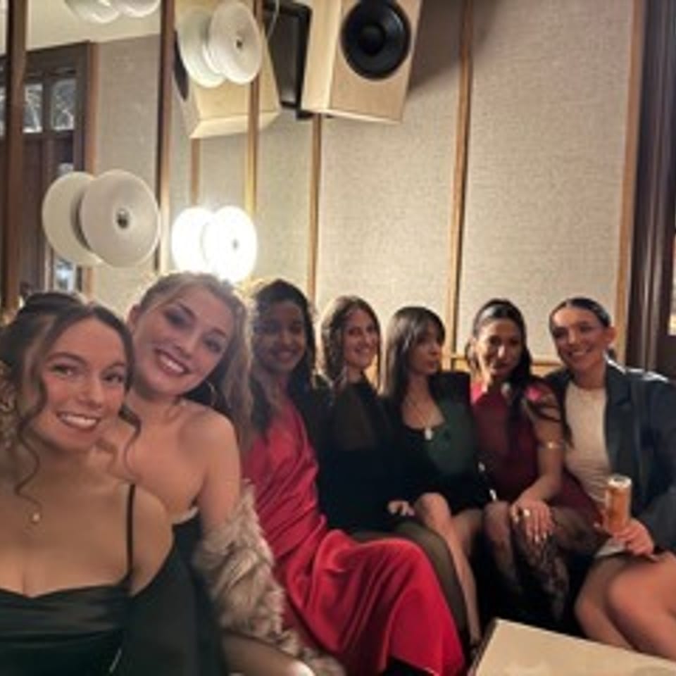 Group of smiling women pose together in a warmly lit restaurant dining room.